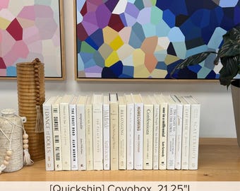 May include: A collection of twenty-one books with cream-colored spines arranged in a row, featuring black text titles. The set is labeled as a Covobox measuring 21.25 inches in length, positioned near a tall wooden vase and a beaded decorative object.