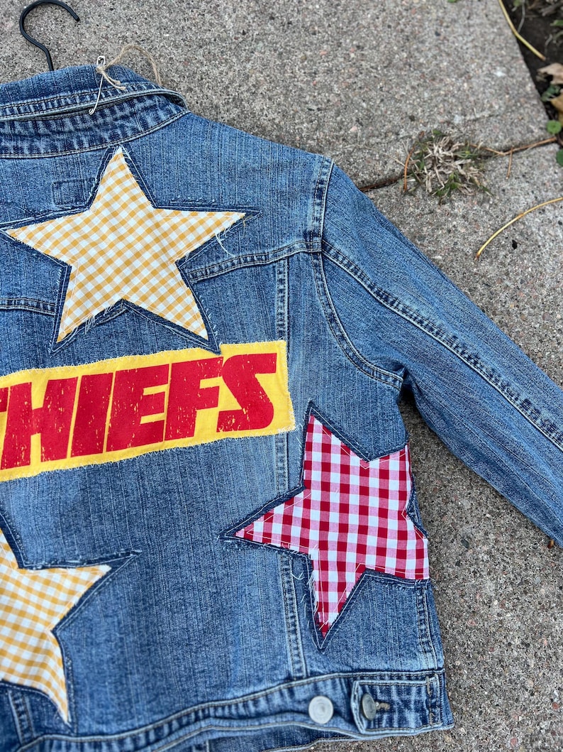 Peut inclure: Veste en jean bleue avec des &eacute;cussons en forme d'&eacute;toile en vichy jaune et vichy rouge et blanc. Le mot "CHIEFS" est imprim&eacute; en rouge sur un fond jaune au dos de la veste.