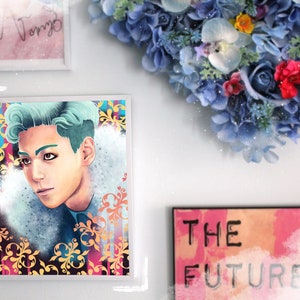 May include: A framed print of a man with teal hair, wearing a blue and white patterned shirt, against a background of colorful floral designs. The print is surrounded by a white frame.