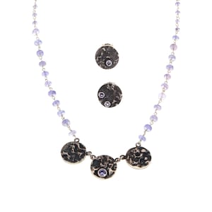 May include: A silver necklace with a chain of small lavender beads and three larger round pendants with textured surfaces and small lavender stones. The necklace has a silver clasp.