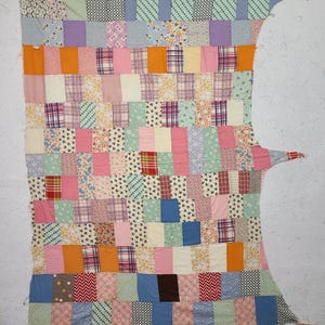 May include: A patchwork quilt with a variety of fabric patterns and colors. The quilt features squares and rectangles in shades of pink, orange, blue, green, and floral prints. The quilt has an irregular shape with extended edges.
