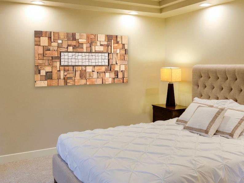 The statement piece is on the light-coloured side wall of a bedroom. It is created with pieces of recycled wood of different shapes and sizes. It is painted in warm tones and the central part has pieces different from the rest. Dimensions: 48 x 24 in