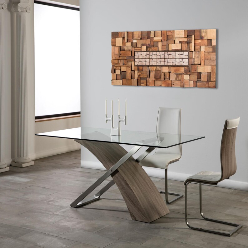 May include: A modern dining room set featuring a glass-top table with a unique wooden and metal base. Two chairs with white leather seats and wooden backs are positioned around the table. A wooden art piece hangs on the wall, and a candle holder with three candles sits on the table.