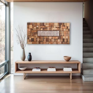 May include: A large, rectangular wooden wall art piece composed of various sized wood blocks in shades of brown. A rectangular section in the center features a grid pattern. The artwork hangs above a light wood console table with decorative items.