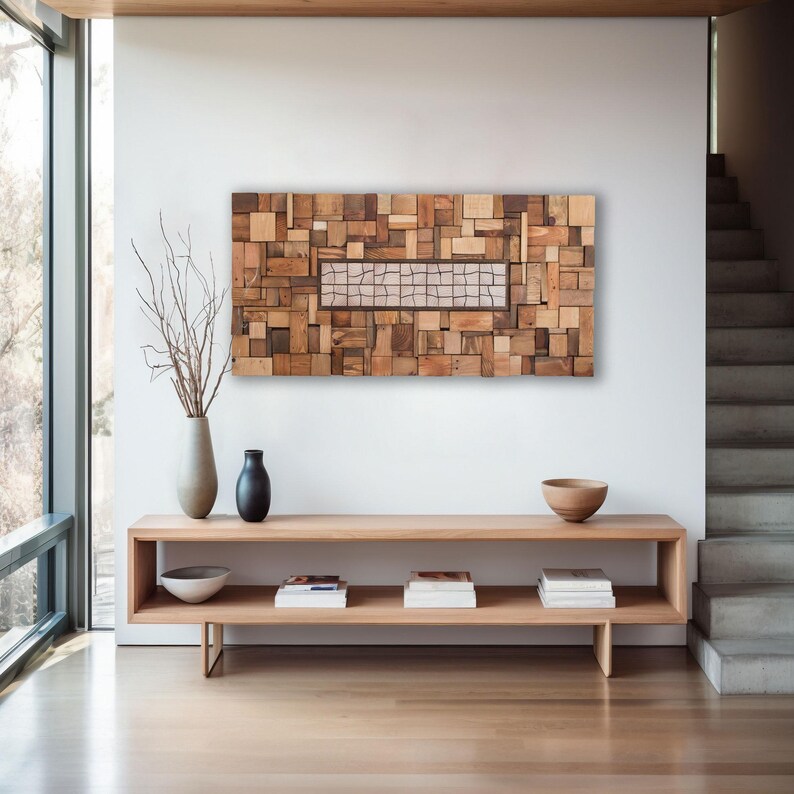 May include: A large, rectangular wooden wall art piece composed of various sized wood blocks in shades of brown. A rectangular section in the center features a grid pattern. The artwork hangs above a light wood console table with decorative items.