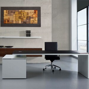 The wood wall art is placed on the wall of a modern and elegant office. Its dimensions are: 48 x 24 inches. The interior has a relief composition of recycled wood pieces of different shapes and shades. Around it is a narrow area painted in dark brown