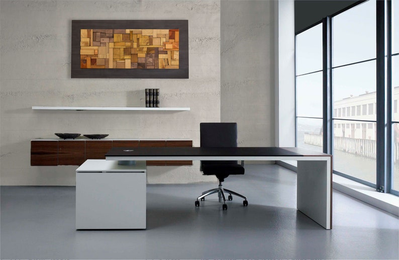The wood wall art is placed on the wall of a modern and elegant office. Its dimensions are: 48 x 24 inches. The interior has a relief composition of recycled wood pieces of different shapes and shades. Around it is a narrow area painted in dark brown