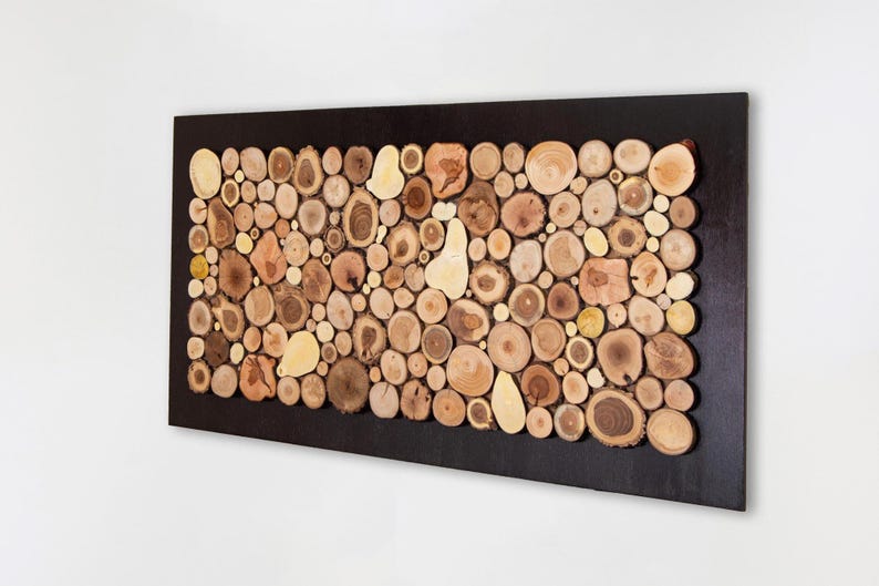 Puede incluir: Una pieza de arte mural rectangular con un marco marr&oacute;n oscuro relleno de numerosas rodajas de madera circulares de diversos tama&ntilde;os en tonos naturales beige, marr&oacute;n y crema. Las piezas de madera est&aacute;n dispuestas para crear un mosaico.