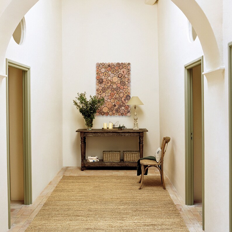 May include: A hallway with white walls and a wooden console table with a decorative wood circle wall art piece above it. The console table has two baskets and a lamp on it. There is a chair in the hallway and a rug on the floor.