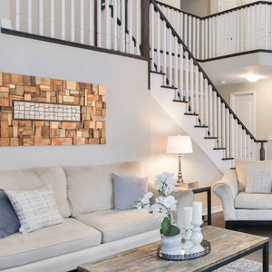 The textural wall art is on the wall of a living room on a sofa. It is created with pieces of recycled wood of different shapes and sizes. It is painted in warm tones and the central part has different pieces from the rest. Dimensions: 48 x 24 in.
