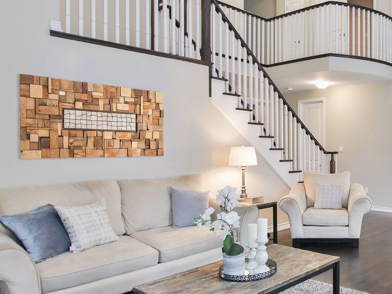 The textural wall art is on the wall of a living room on a sofa. It is created with pieces of recycled wood of different shapes and sizes. It is painted in warm tones and the central part has different pieces from the rest. Dimensions: 48 x 24 in.