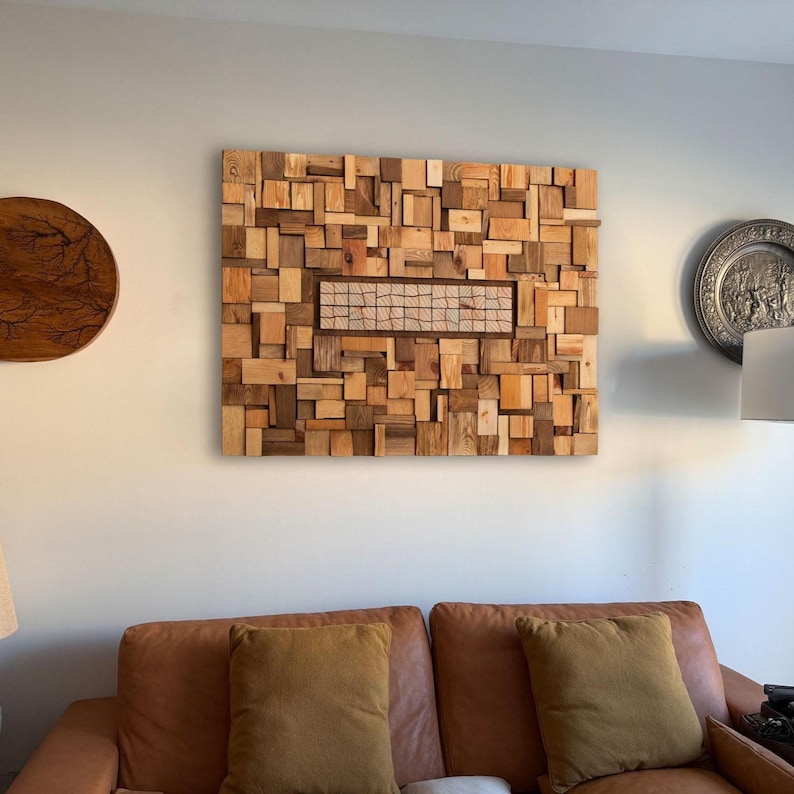 May include: A large, rectangular wooden wall art piece composed of various sized wood blocks in shades of brown and tan. A rectangular section in the center features a woven pattern. The artwork is mounted on a light-colored wall.