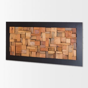 The artwork is in a horizontal position. Its dimensions are: 48 x 24 in. The interior has an in relief composition of recycled wood pieces of different shapes and tones. Around it is a narrow area painted dark brown. It is a modern and original piece