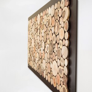 Side image. It is a work created with slices of tree branches. The thickness of the slices can be seen (1 in. approx.) The slices occupy almost the entire surface and the exterior of 2 in. approx. is painted in dark brown. Size: 48 x 24 in.