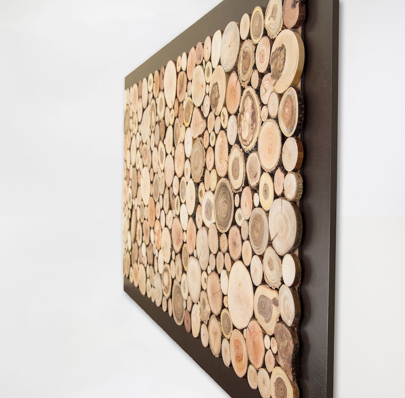 Side image. It is a work created with slices of tree branches. The thickness of the slices can be seen (1 in. approx.) The slices occupy almost the entire surface and the exterior of 2 in. approx. is painted in dark brown. Size: 48 x 24 in.