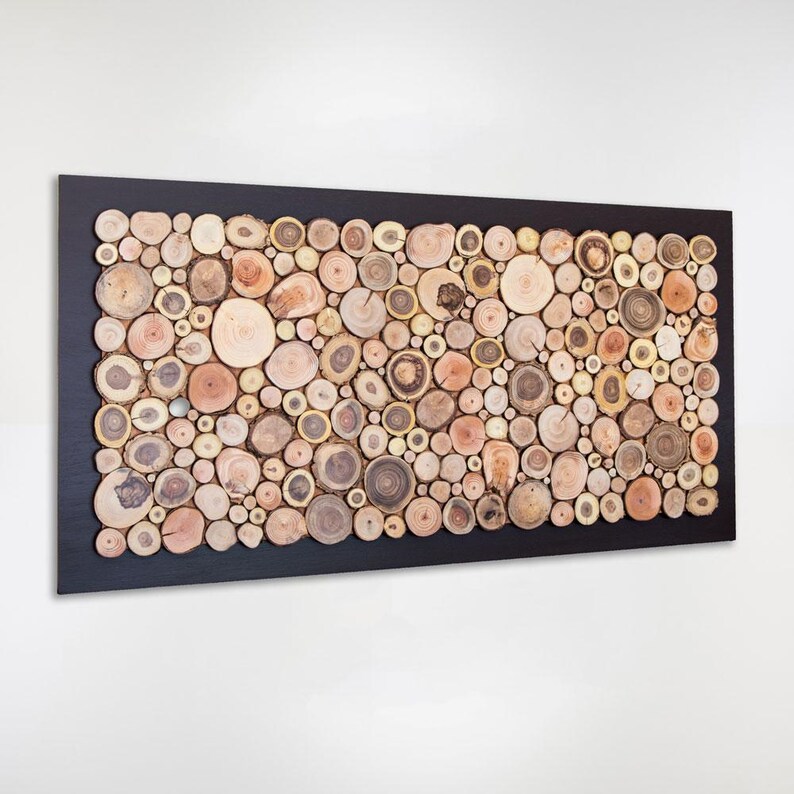 Puede incluir: Una pieza de arte mural rectangular con un marco negro relleno de numerosas rodajas de madera circulares de diversos tama&ntilde;os y tonos marrones claros naturales. Las piezas de madera est&aacute;n dispuestas juntas para crear una superficie de mosaico texturizada.