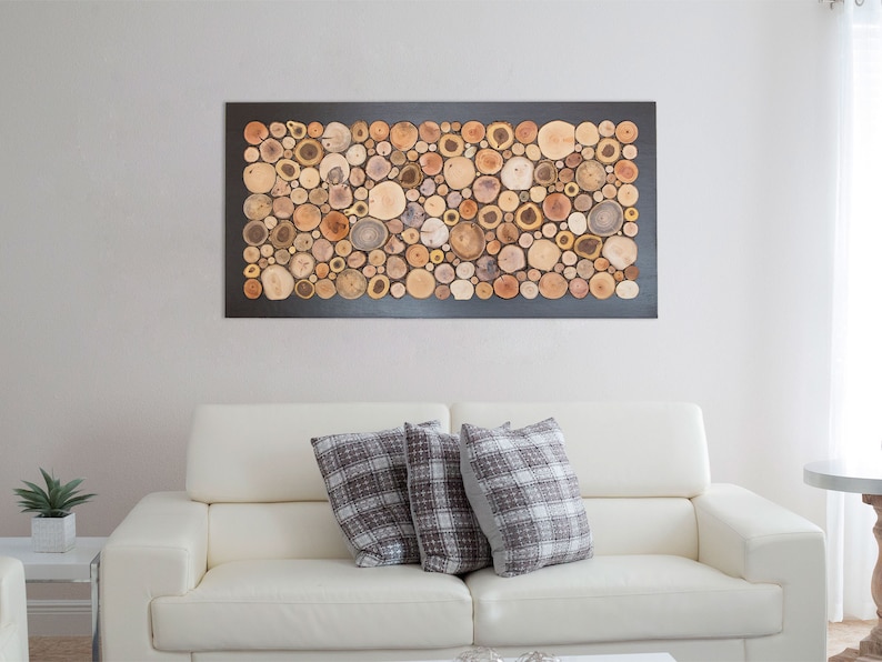 May include: A rectangular wall art piece featuring a mosaic of numerous circular wood slices in various shades of brown, tan, and cream. The wood slices are arranged closely together and mounted within a solid black rectangular frame.