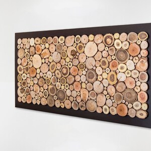 Side image. This is a beautiful and elegant wall sculpture created from slices of tree branches of different shades. The slices take up almost the entire surface and the 2 in exterior is painted dark brown. Size: 48 x 24 in. Can be personalised
