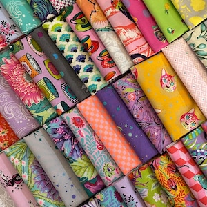 May include: A selection of rolled fabric bolts featuring diverse, colourful patterns. Designs include floral, geometric, and illustrations of cats, teacups, and birds. The fabrics are in shades of pink, green, purple, and yellow.