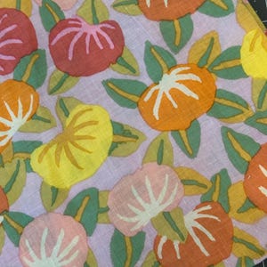 May include: A fabric textile featuring a repeating floral pattern with stylised round blossoms in shades of orange, red, yellow, and pink. The flowers are accented with white line details and surrounded by green leaves on a light lavender background.