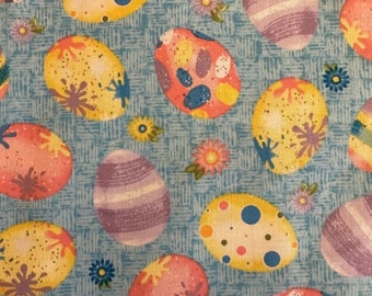 May include: A blue fabric with a repeating pattern of colorful Easter eggs. The eggs are decorated with dots, stripes, and swirls.