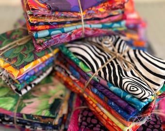 May include: Stacks of colorful fabric squares tied with twine. The fabrics feature a variety of patterns, including floral, zebra stripes, and abstract designs. The color palette includes vibrant hues like pink, orange, purple, green, and blue.