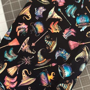 Peut inclure: Un tissu noir avec un motif répétitif d'objets magiques colorés, notamment des chapeaux pointus étoilés, des bottines à lacets dans des tons bleu et rose, des chaudrons bouillonnants, des balais en bois et des baguettes fines aux détails floraux.