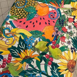 May include: A vibrant fabric featuring a colorful botanical design. The pattern includes sunflowers, oranges, bananas, watermelon, and other fruits and flowers. The color palette is bright, with shades of yellow, green, red, and blue. The fabric has a white background.