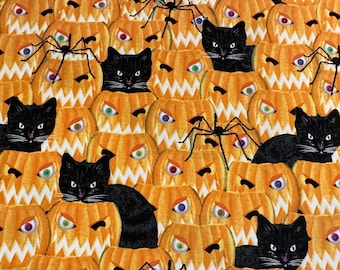 May include: A Halloween-themed fabric with a repeating pattern of orange pumpkins with black cat faces and spider webs. The pumpkins have black eyes and a toothy grin.