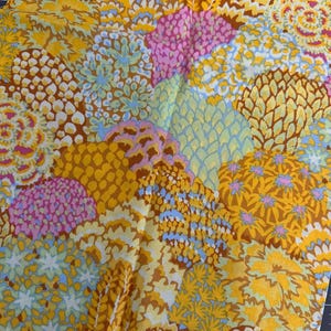 May include: A fabric featuring a dense, repeating pattern of stylised floral and geometric shapes in vibrant shades of yellow, orange, brown, pink, and light blue. The design consists of overlapping circular and fan-like motifs with intricate textures.