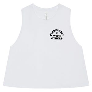 May include: A white sleeveless crop top featuring a round neckline and raw-cut armholes. On the upper left chest, the text "FLOWS WELL WITH OTHERS" is printed in black capital letters, with a small black heart icon positioned between the words.