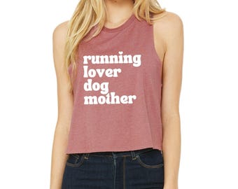 May include: A heathered mauve sleeveless crop top featuring the white text "running lover dog mother" printed in a bold, rounded sans-serif font on the front. The garment has a crew neckline and a relaxed, boxy fit with wide arm openings.