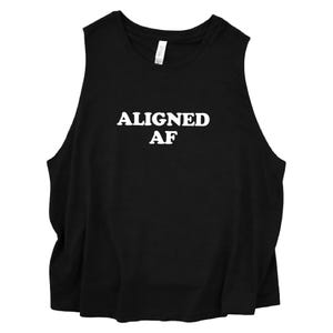 May include: A black sleeveless tank top featuring the white text ALIGNED AF printed in a bold, sans-serif font across the center of the chest. The garment has a round neckline and a relaxed, loose-fitting silhouette with wide arm openings.