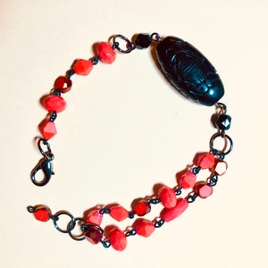 May include: A black bracelet with a carved black bead and red faceted beads.