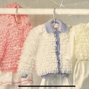 May include: Three baby outfits hanging on a rod. The outfits include a pink jacket, a white jacket with a blue collar, and a yellow jacket. The jackets have a fluffy, textured appearance. The outfits are displayed on hangers.