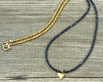 Op de afbeelding: Een gouden en zwarte kralenketting met een gouden hartbedel. De ketting is gemaakt van twee strengen kralen, een gouden en een zwarte.
