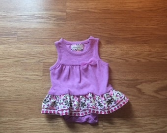 May include: A purple sleeveless dress with a white and pink floral print on the bottom. The dress has a small tag on the front that says "Little Me".