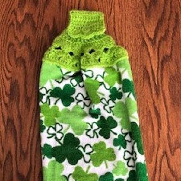 St Patrick’s hanging kitchen towel with a crocheted top.  It has shamrocks in different sizes and colors of green  The tab is  light green.