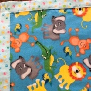 Baby blanket (flannel) with a rolled hemmed border. The blanket has whimsical monkeys, elephants, lions, alligators and birds on a blue back