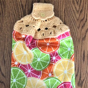 Hanging kitchen towel with a crocheted top.  It has sliced lemons, limes, oranges and grapefruit.  The tab at the top is yellow.