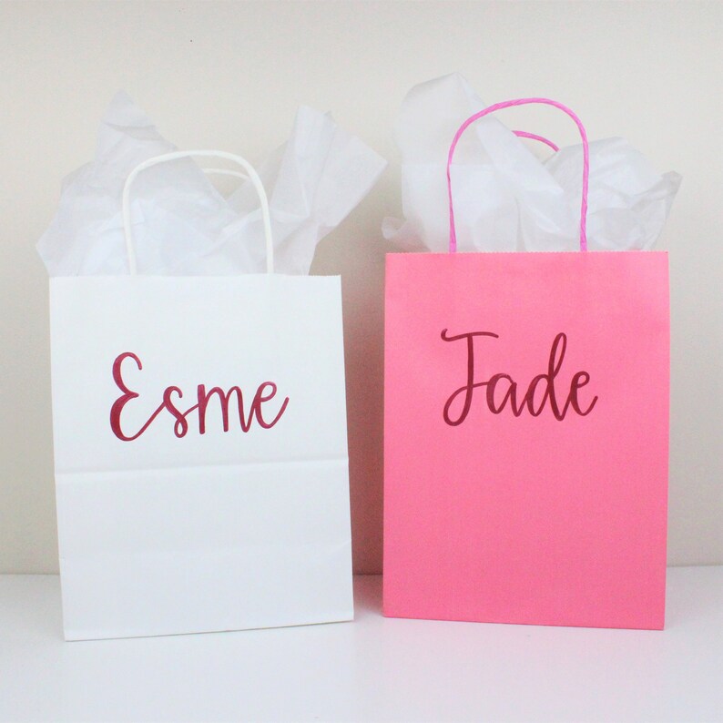 Pu&ograve; includere: Due sacchetti regalo con carta velina all'interno. Un sacchetto &egrave; bianco con il nome "Esme" scritto in rosso. L'altro sacchetto &egrave; rosa con il nome "Jade" scritto in rosso.