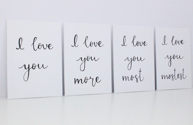 Puede incluir: Cuatro lienzos blancos con caligraf&iacute;a negra que dice "Te amo", "Te amo m&aacute;s", "Te amo m&aacute;s", y "Te amo m&aacute;s que nada".