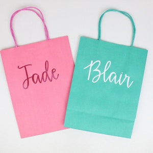 Pu&ograve; includere: Due sacchetti regalo di carta, uno rosa con il nome "Jade" in lettere rosa e uno verde acqua con il nome "Blair" in lettere bianche.