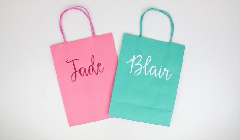 Pu&ograve; includere: Due sacchetti regalo di carta, uno rosa con il nome "Jade" in lettere rosa e uno verde acqua con il nome "Blair" in lettere bianche.