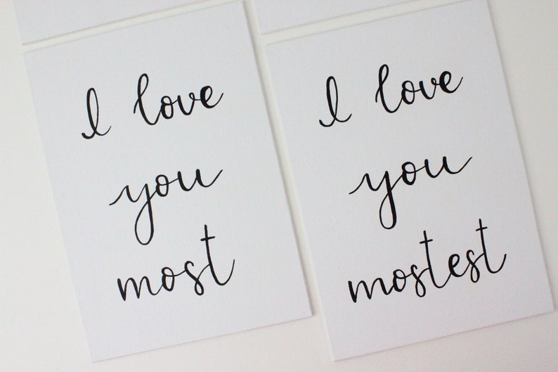 Puede incluir: Dos tarjetas blancas con caligraf&iacute;a negra que dice "Te amo m&aacute;s" y "Te amo m&aacute;s".