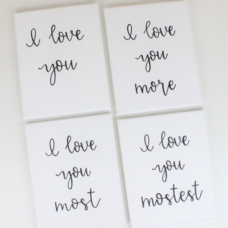 Puede incluir: Cuatro lienzos cuadrados blancos con caligraf&iacute;a negra que dice "Te amo" en cada lienzo. El texto en los lienzos dice "Te amo", "Te amo m&aacute;s", "Te amo m&aacute;s", y "Te amo m&aacute;s que todo".