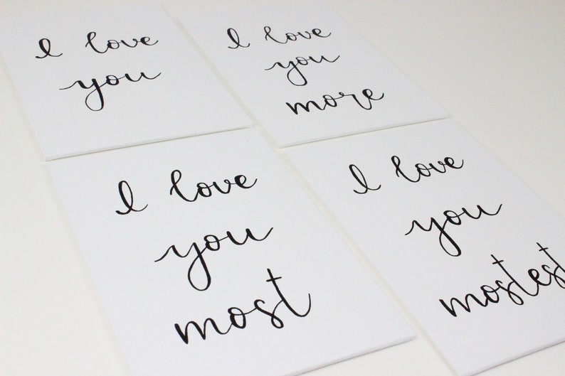 Puede incluir: Cuatro lienzos blancos con caligraf&iacute;a negra que dice "Te amo", "Te amo m&aacute;s", "Te amo m&aacute;s", y "Te amo m&aacute;s que nada".