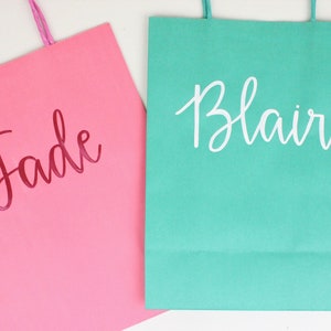 Pu&ograve; includere: Due sacchetti regalo, uno rosa con il nome "Jade" in lettere rosse e uno verde acqua con il nome "Blair" in lettere bianche.
