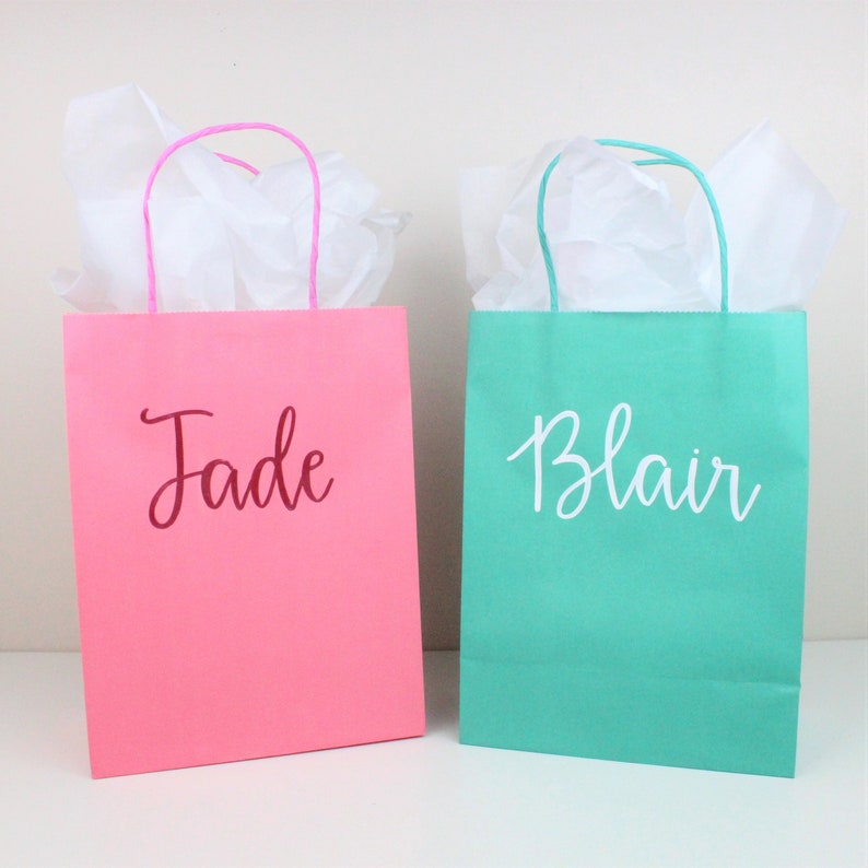 Pu&ograve; includere: Due sacchetti regalo con carta velina all'interno. Il sacchetto a sinistra &egrave; rosa con il nome "Jade" scritto in marrone. Il sacchetto a destra &egrave; turchese con il nome "Blair" scritto in bianco.