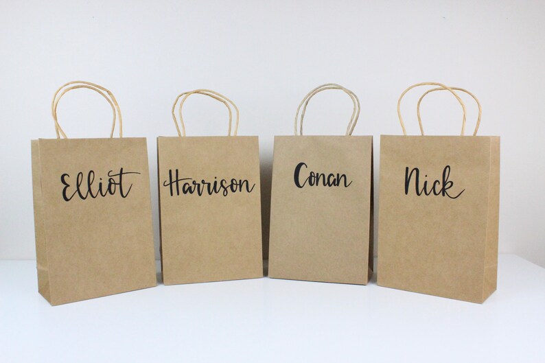 May include: Four brown paper gift bags with handles. Each bag has a name written on the front in black script: Elliot, Harrison, Conan, and Nick.
